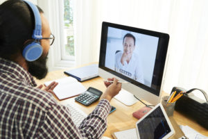 Happy Asian businessman in computer screen talking online to his colleague in office sitting in front of monitor